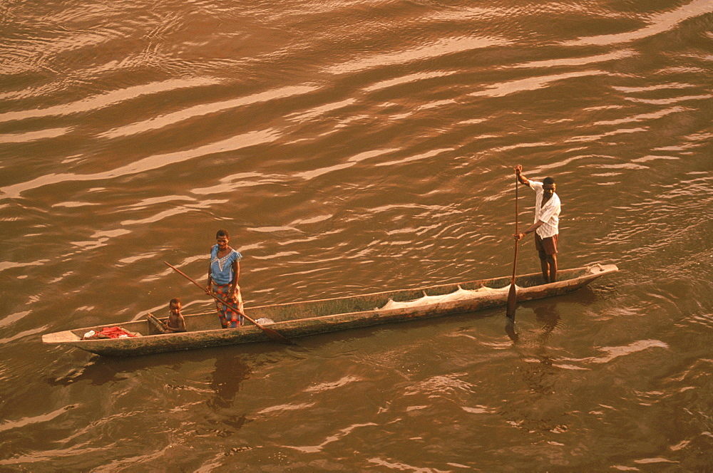 A family in their dugout canoe or pirogue paddles across the brown water of the Congo River.