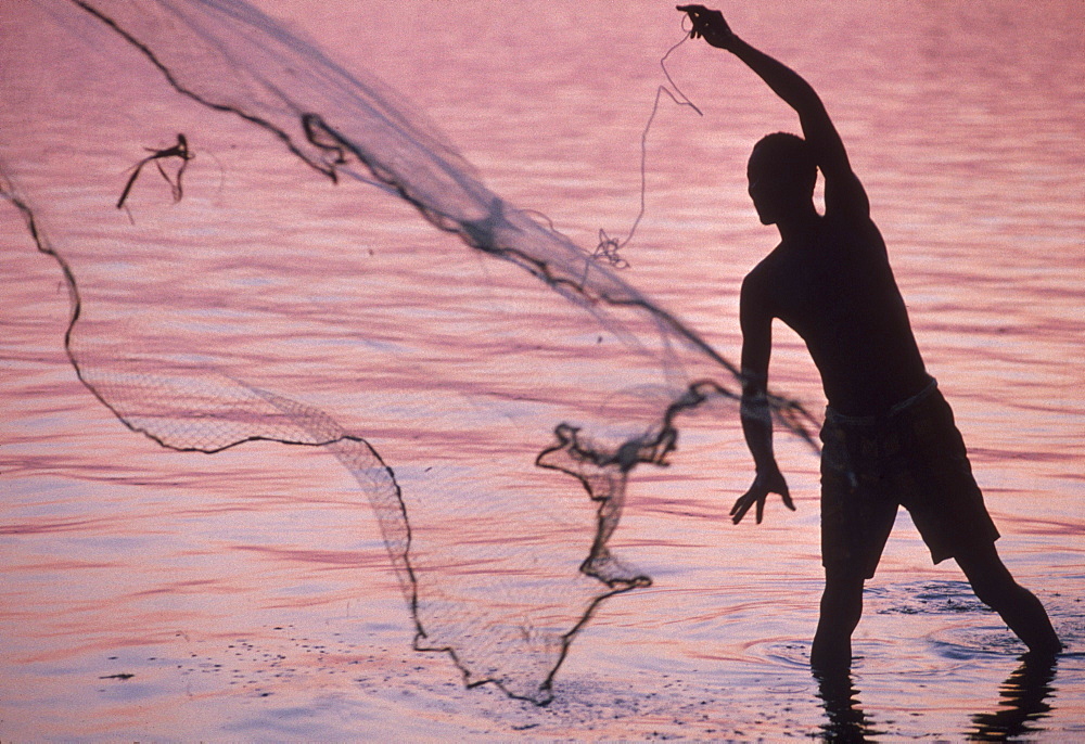 Fisherman throws a cast net into the Congo River at sunset.