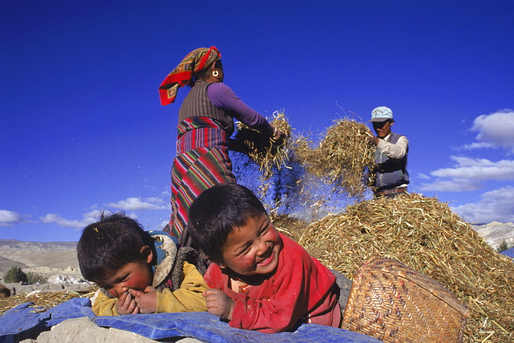 Children laugh as their parents winnow wheat on their farm near Lo Manthang, capital of the Kingdom of Mustang, Nepal.