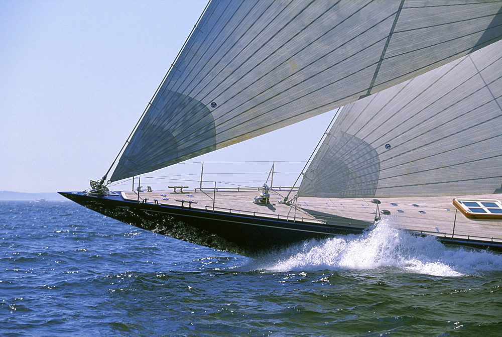 A traditional racing yacht, a 130 foot J-Class Sloop, sails ahead.