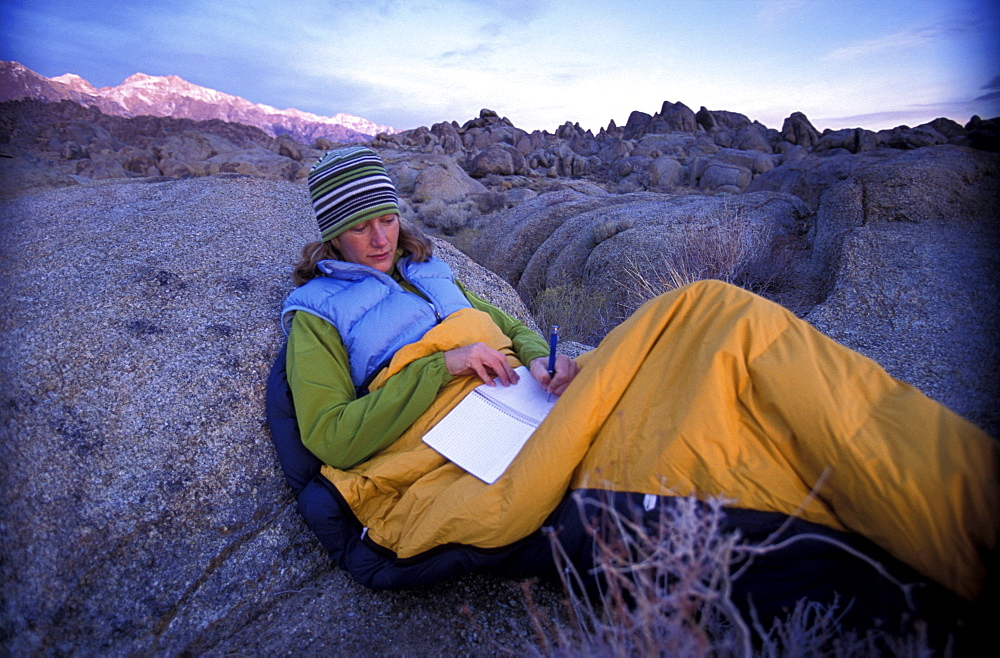 Ashley Laux reads and writes in her notebook while sitting in her sleeping bag to stay warm in the early morning while camping in the Alabama Hills near Lone Pine in the Eastern Sierra Nevada mountains, California.