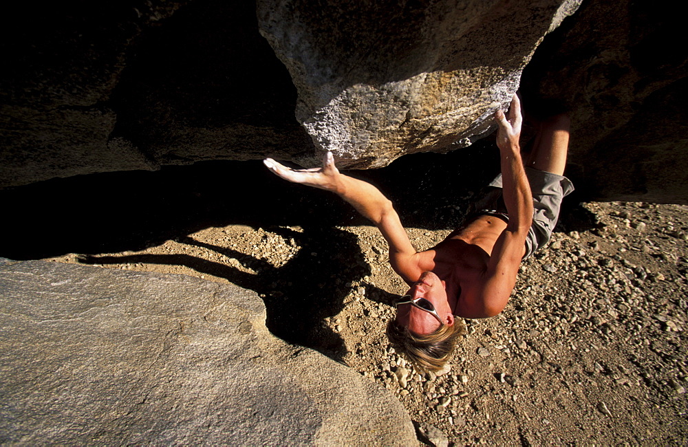 A high angle view of Kevin Swift climbing on an overhanging boulder in the Buttermilks, California, near Bishop in the Eastern Sierra Nevada mountains..