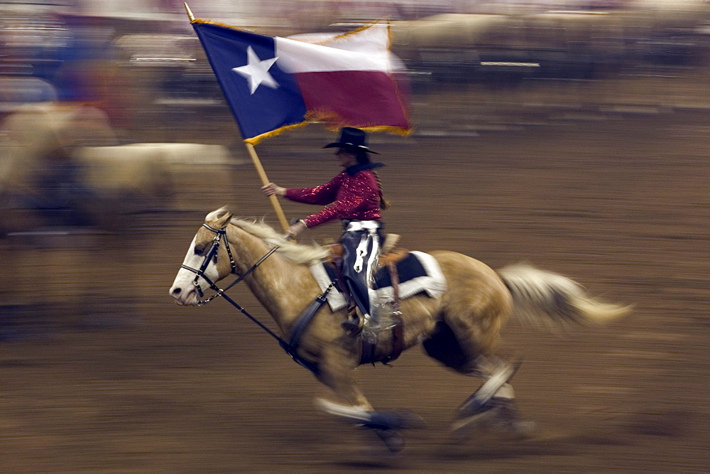 Young cowboy trotting in the arena holding a Texas flag at the San Antonio Rodeo Show.