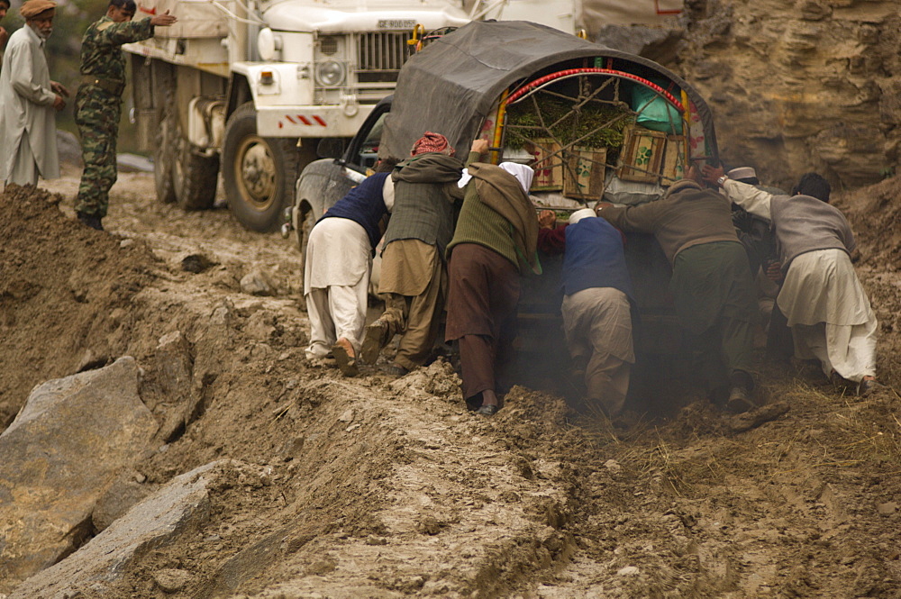 On the the road to the Allai Valley, men try to push a truck  that is stuck in mud and landslide debris and which is blocking other trucks full of humanitarian aid and  earthquake survivors returning to their  mountain villages, Battagram District, Pakistan's Northwest Frontier Province.  The region was one of the worst-hit by the October 2005 earthquake, and aftershocks and  heavy rains continue to trigger landslides, which have hampered reconstruction efforts and the return of earthquake survivors  to their mountain villages from the low altitude tent camps where many spent the winter.