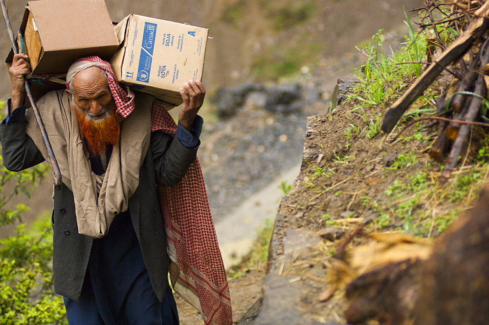 A Pashtun man returning home to his mountain home from a camp for earthquake survivors, carries boxes up a steep hill, in the Battagram District, Pakistan's Northwest Frontier Province.  The Pakistan army has dictated that all camps for people displaced by the earthquake be emptied by early April, whether families want to return or not.  The Battgram district was one of the worst-hit by the October 2005 earthquake, and aftershocks and  heavy rains continue to trigger landslides, which have hampered reconstruction efforts and the return of earthquake survivors  to their mountain villages from the low altitude tent camps where many spent the winter.