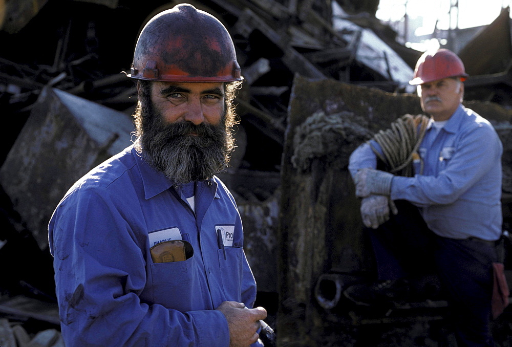 Two oil refinery workers wearing red helmets stands outside for a smoke.