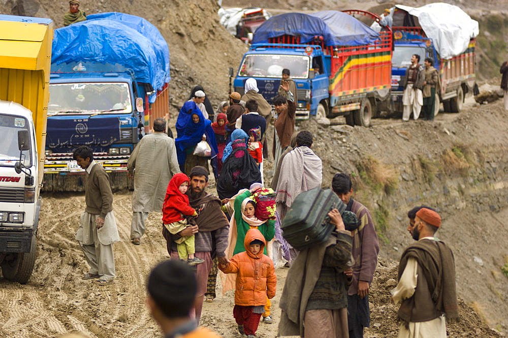 On the the road to the Allai Valley, a Pashtun family carries luggage past trucks that are stuck in mud and landslide debris-the trucks are full of  other  families and their possessions traveling back to their mountan villages, Battagram District, Pakistan's Northwest Frontier Province.  The region was one of the worst-hit by the October 2005 earthquake, and aftershocks and  heavy rains continue to trigger landslides, which have hampered reconstruction efforts and the return of earthquake survivors  to their mountain villages from the low altitude tent camps where many spent the winter.