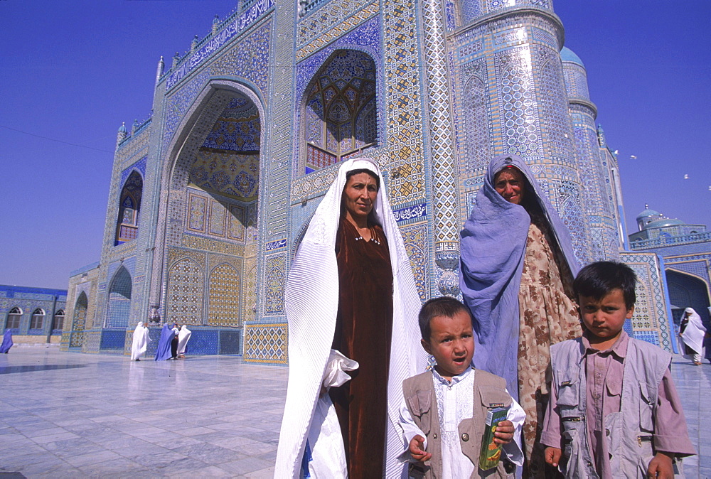 Tajik women proudly pose with their children, burqa's thrown back, in front of the main entrance to the Blue Mosque, Mazar-i-Sharif, Balkh Province.  Wednesday mornings are reserved for women to come and worship at the mosque. Elaborate tilework and decorated spires adorn the mosque, also known as the Shrine of Hazrat Ali (Hazrat Ali was the son-in-law of the prophet Mohammed), who is believed to be buried here.  The shrine, of particular importance for Afghanistan's Shi'ite Muslims, was first built in the 12th century, destroyed by Genghis Khan, and rebuilt in 1481.  The current mosque, considered by some to be one of the most beautiful in Central Asia, is a modern restoration.