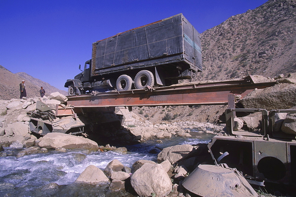 A truck  drives over a makeshift bridge supported by ruined tanks on the road north of the Salang Tunnel in Baghlan province, August 31, 2002.  High  in the mountains of the Hindu Kush, the road was destroyed several years ago by a flood from raging mountain rivers.  The road was improved  by the Soviets after their 1979 invasion of Afghanistan, and was a crucial link for troops and supplies coming from the Soviet Union.  The mountain road is in terrible condition, and its repair is crucially important for the reconstruction of the country