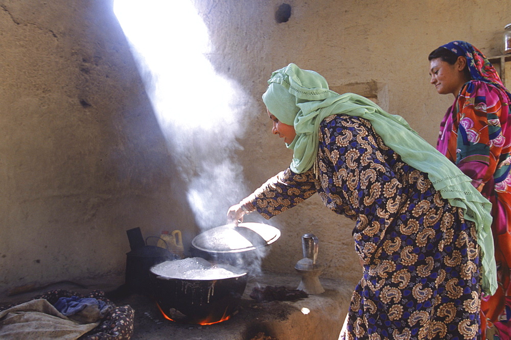 Young Tajik women cook on clay stove in the compound of an extended family in Mazar-i-Sharif, Balkh Province.  The kitchen is open air, with wood fires stocking clay ovens and stoves, which allow several huge pots to be simmering at once.