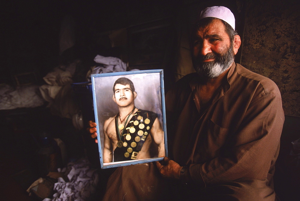 An Afghan man holds a portait of himself as an Olympic wrestler in one of the old bazaars of Kabul.  The man, now working as a traditional healer in a tiny stall, had been part of the Afghan Olympic team in the 1970's and had competed in Europe and in Mexico City.