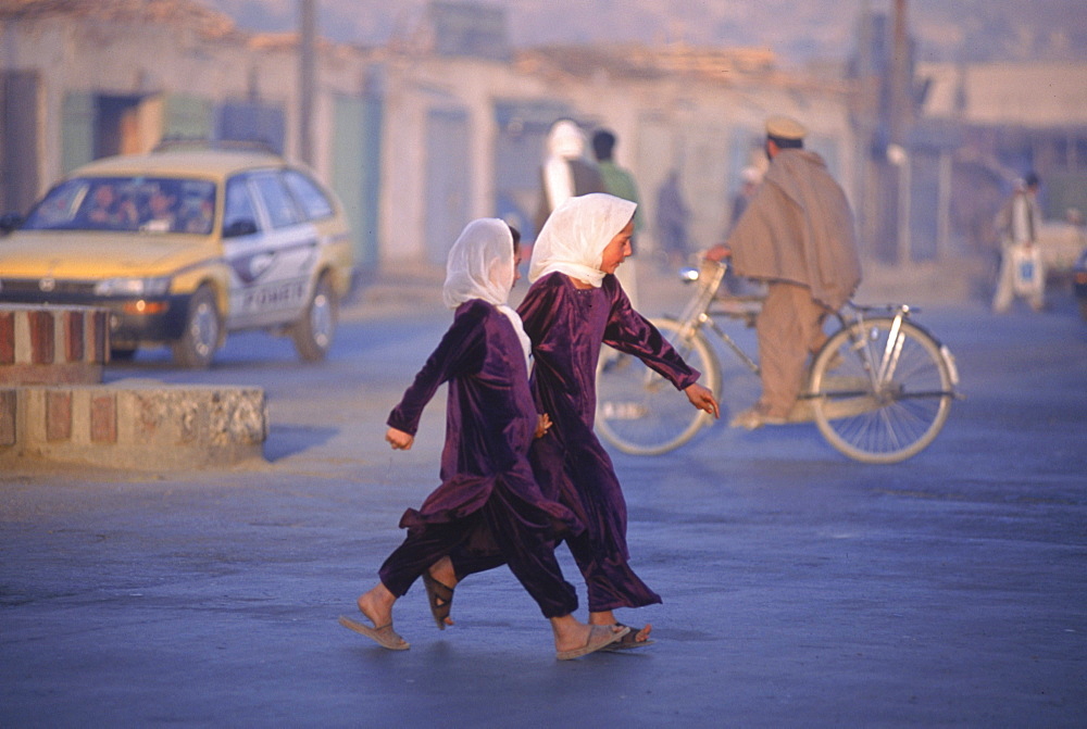 Two school girls hurry across a street at dawn in Kabul, Afghanistan.  Since the fall of the Taliban, a record number of girls have returned to school throughout Afghanistan. Much of Kabul  was  destroyed in the mid 1990's (1992-1996) in factional fighting between rival mujahideen commanders for control of the capital after the Soviet's withdrawal, and now Afghans are re-building their lives and business