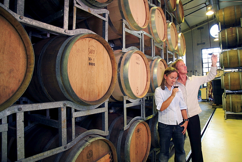 Young couple in their late 20's taste wines in the wine cellar at West Brook Wines in Kumeu, West Auckland, while looking at the stacks of barrels of ageing wines.