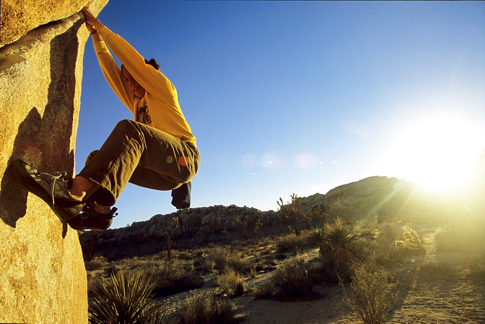 Dana Ikeda boulders The Tube in Joshua tree national park with the sun at sunset bursting behind her.