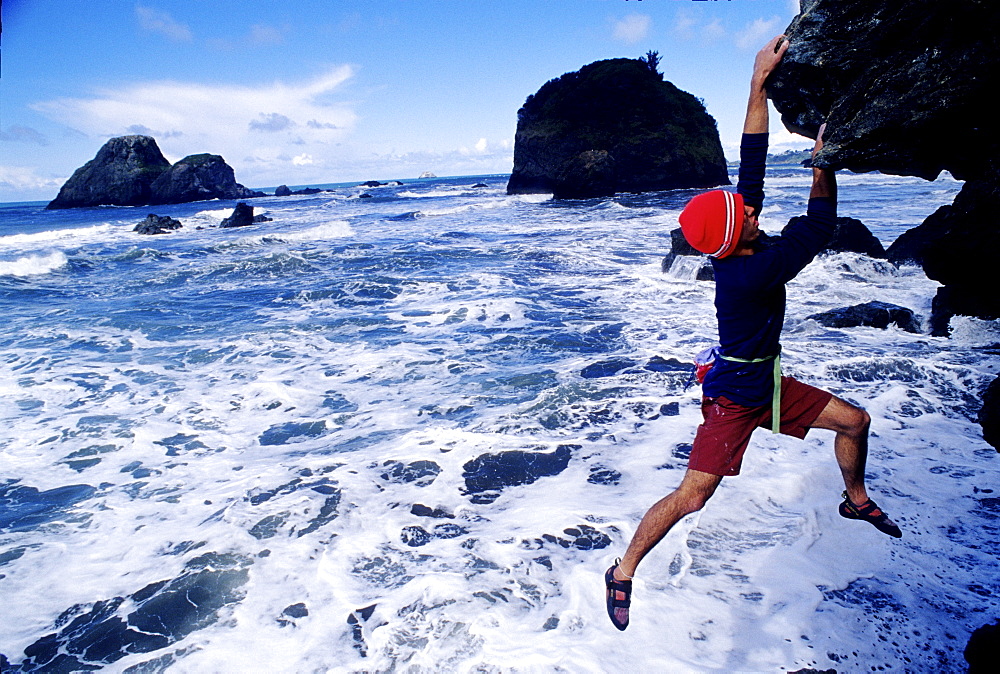 A boulderer hanging above the beach in evening in Northern California.