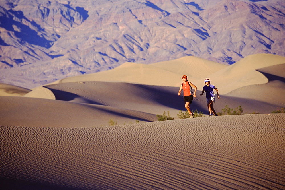 Two women running on a sand dune in Death Valley, California.