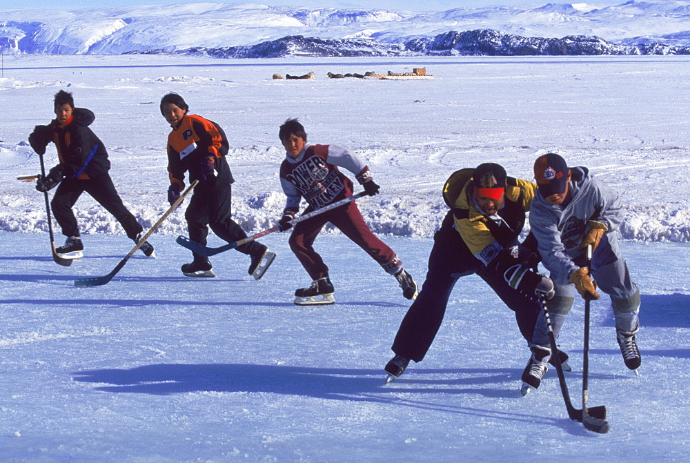 Kids playing hockey on ice in front of the town. An indoor rink is being built so they can play in the summer and during long cold winter months.