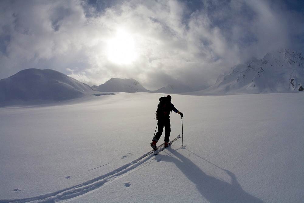 Backcountry skier crosses glacier under late day stormy sky.