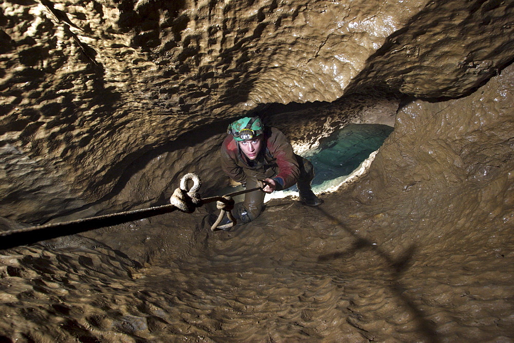 Cave explorer ascends a knotted rope out above a pool of water in a cave in England called Streaks Pot.