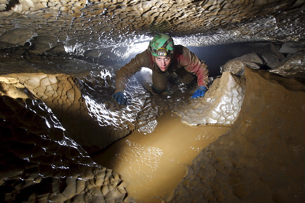 Cave explorer crawls through a low section of cave passage underground in Derbyshire England.