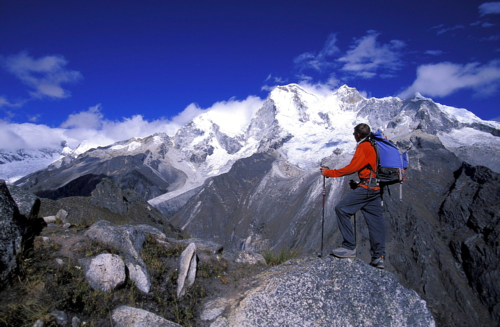 Man standing on a peak looking out at snow covered mountains in Cordillera Blanca, Peru.