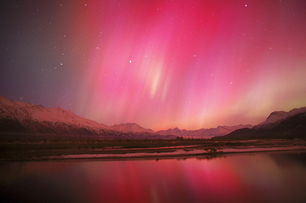 The aurora borealis (northern lights) shines with pink hues above the Chugach Mountains in Alaska's Knik River Valley.