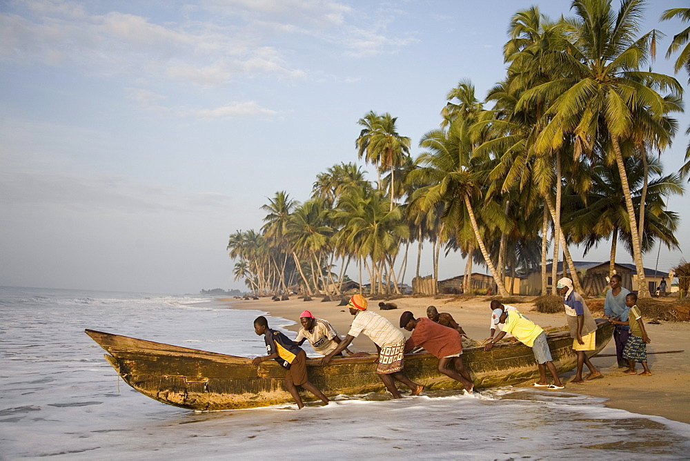 Fishermen pushing a boat into the ocean in Ghana