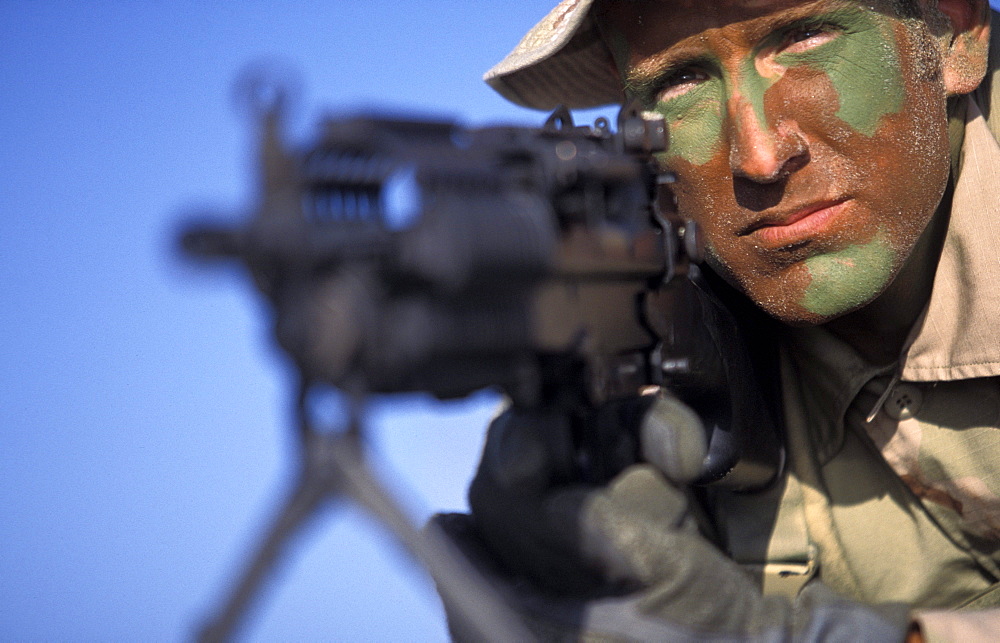 Navy Seal in training laying on the beach aiming a gun in San Diego, California.