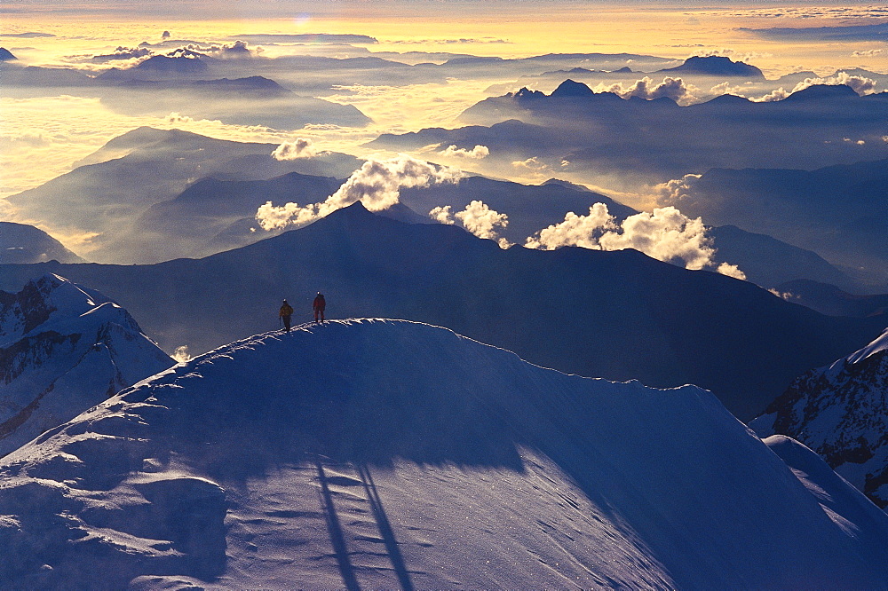 Two climbers at the top of a summit in the Alps.