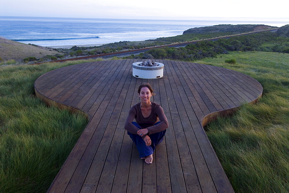 A yong woman watches the sunset from a deck overlooking the Pacific Ocean at Hollister Ranch, California.