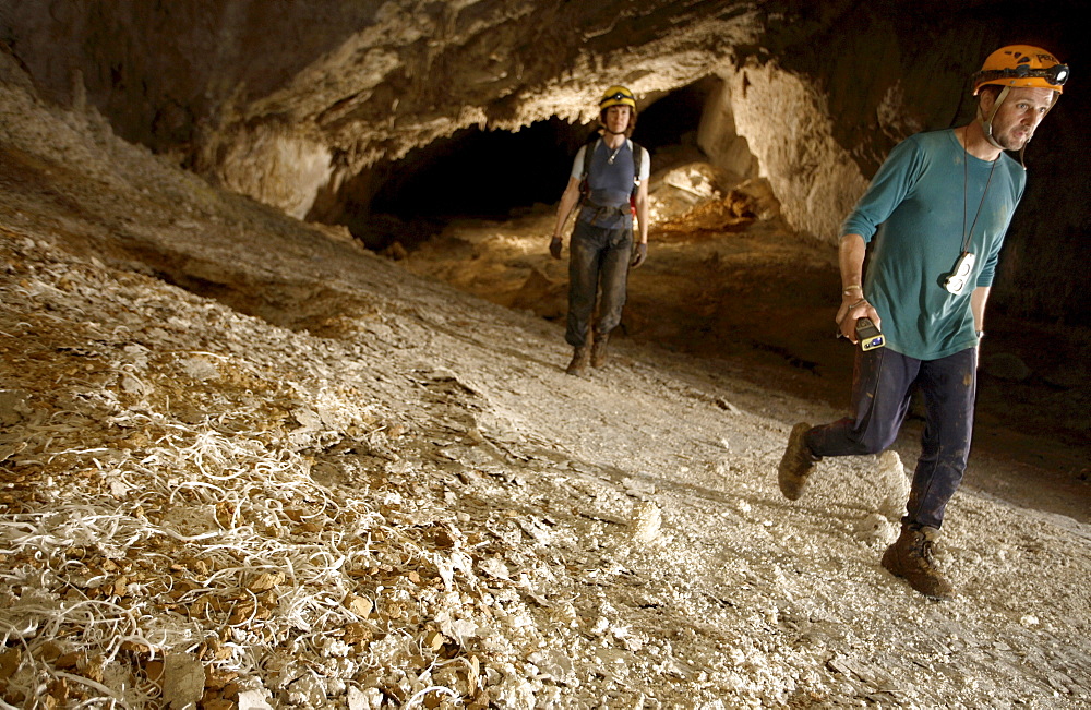 Two cave explorers walk through a section of cave tunnel deep in heart of the mountain. At this point in the cave the floor was