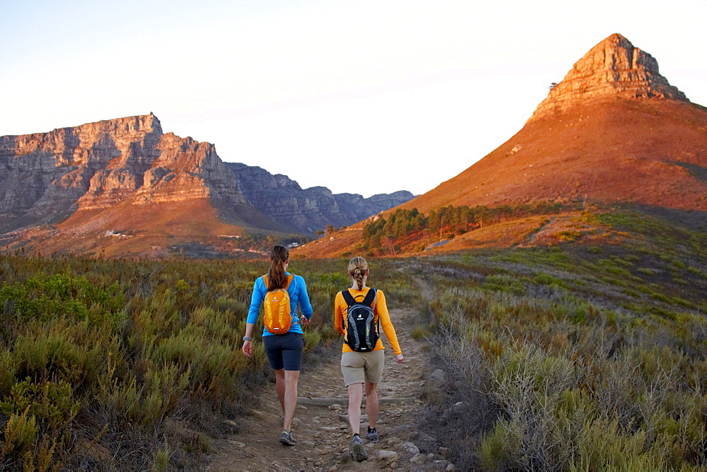 Katrin Schneider and Susann Scheller walking on the trail between Signal Hill and Lion's Head above the city of Cape Town just after sunrise. Cape Town, South Africa.