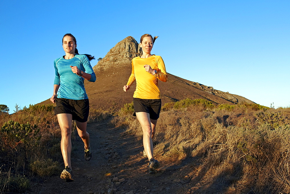 Katrin Schneider and Susann Scheller running on the trail from Lion's Head to Signal Hill above the city of Cape Town just after sunrise. Cape Town, South Africa.