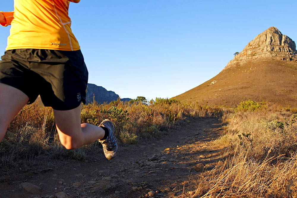 Katrin Schneider running on the trail from Lion's Head to Signal Hill above the city of Cape Town just after sunrise. Cape Town, South Africa.