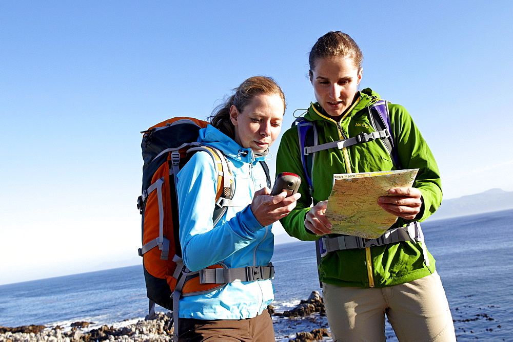 Katrin Schneider and Susann Scheller checking a handheld GPS device while hiking on an ocean trail between Gansbaai and De Kelders. South Africa.