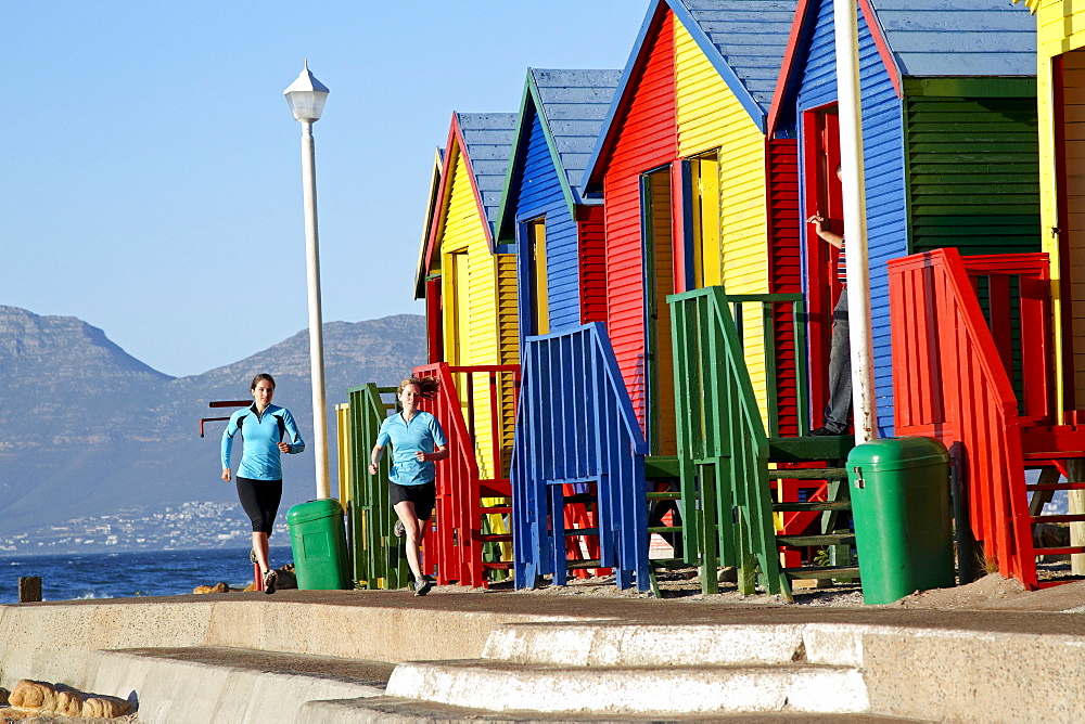 Katrin Schneider and Susann Scheller running past the famous and colorful bathing huts in St.James near Muizenberg. Cape Town, South Africa.