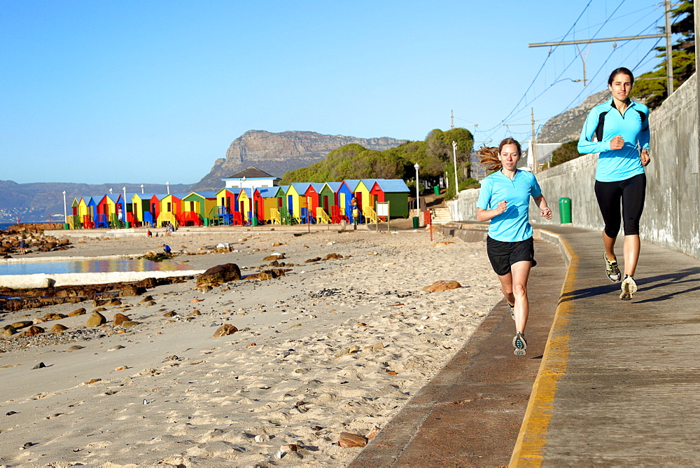 Katrin Schneider and Susann Scheller running past the famous and colorful bathing huts in St.James near Muizenberg. Cape Town, South Africa.