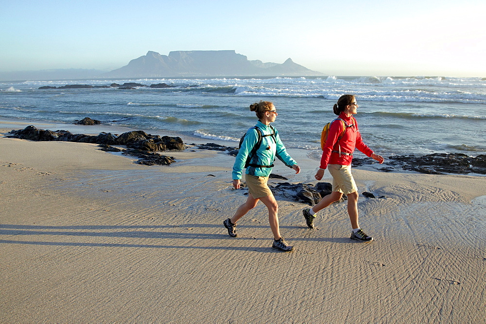 Katrin Schneider and Susann Scheller hiking along Bloubergstrand beach in Cape Town with a perfect view of Table Mountain in the back. Cape Town, South Africa.