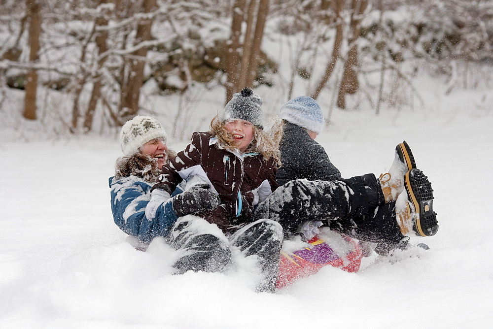 A woman and two children laugh while sledding in deep, powdery snow.