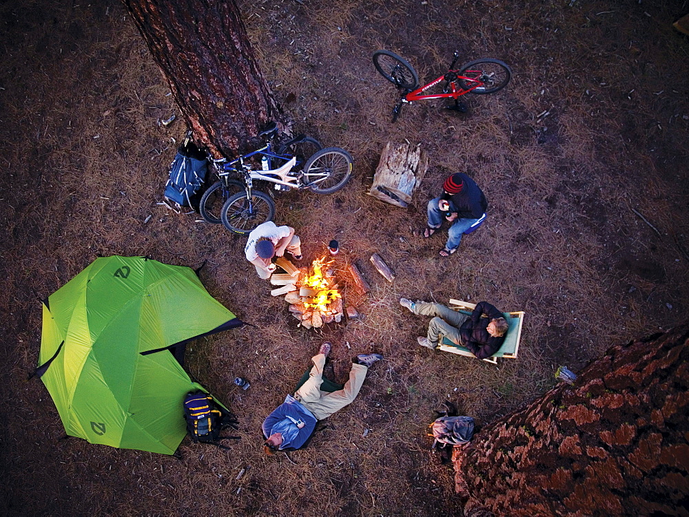 Friends gather outside their tent around the camp fire at a picnic on the beach.