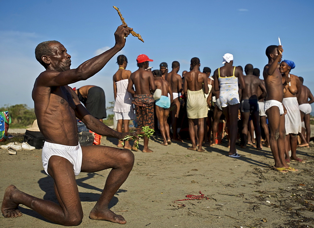 A man kneels in the sand while holding up an offering to the spirits during a voodoo festival on a beach in Haiti.