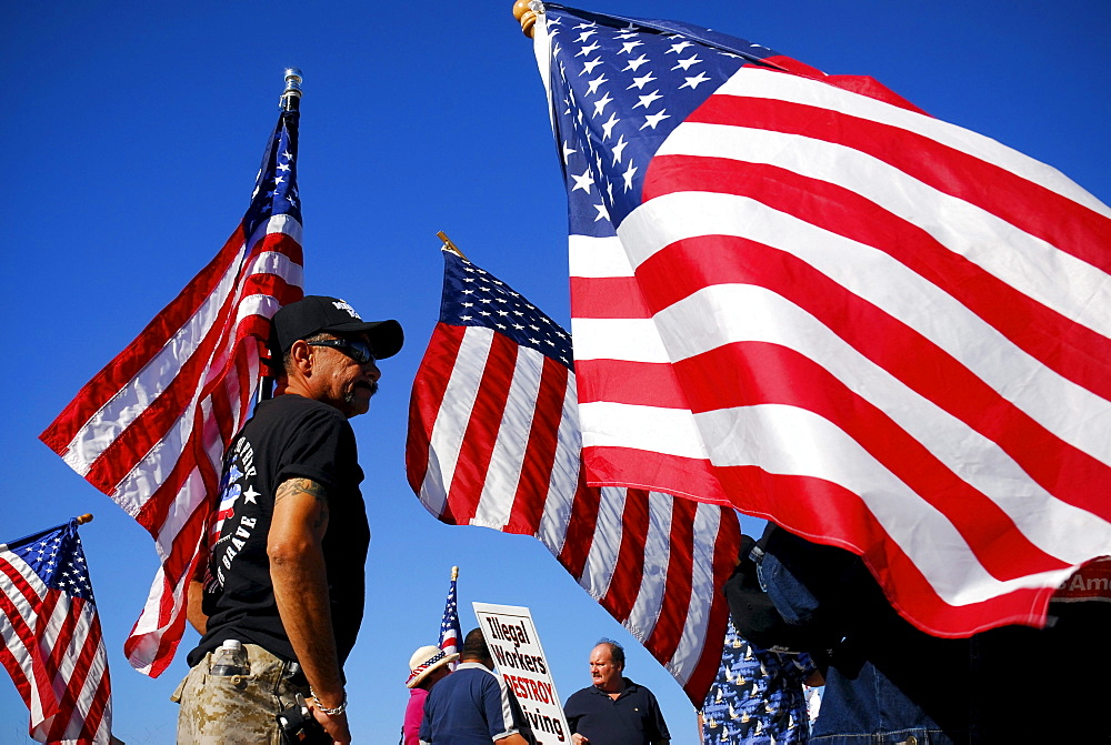 An immigration activist stands surrounded by waving American flags at a Minute Men ralley in San Diego, California.