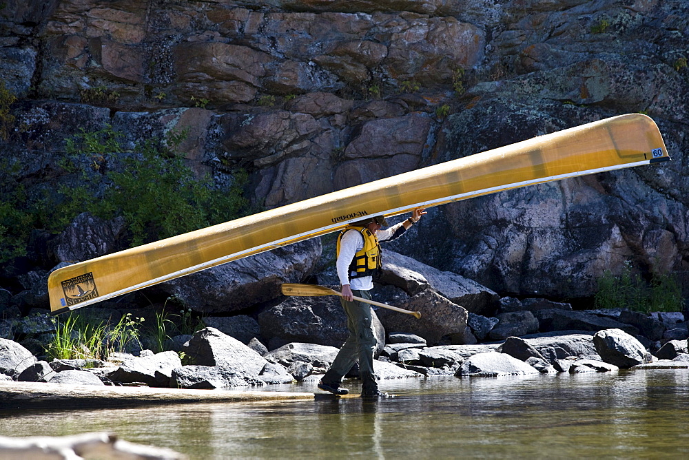 A young water enthusiast carries his canoe on his head while entering the Boundary Waters of Minnesota.