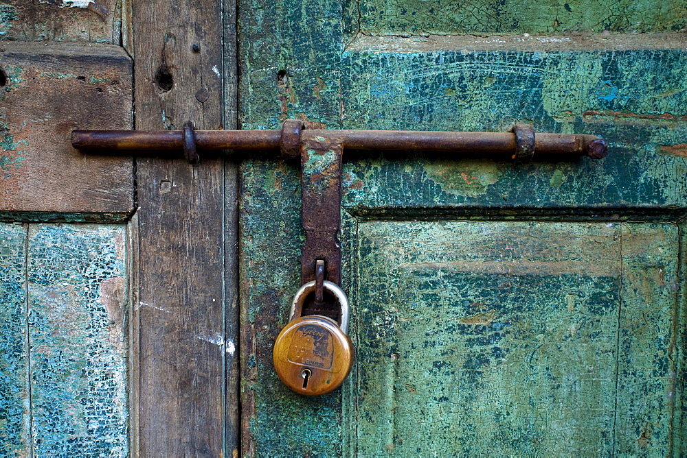 A close up photo of a brass lock on an old blue green shop door.