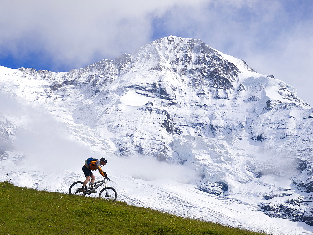 A Mountain biker is descending a grassy ridge in front of the Moench mountain (4099 meter).