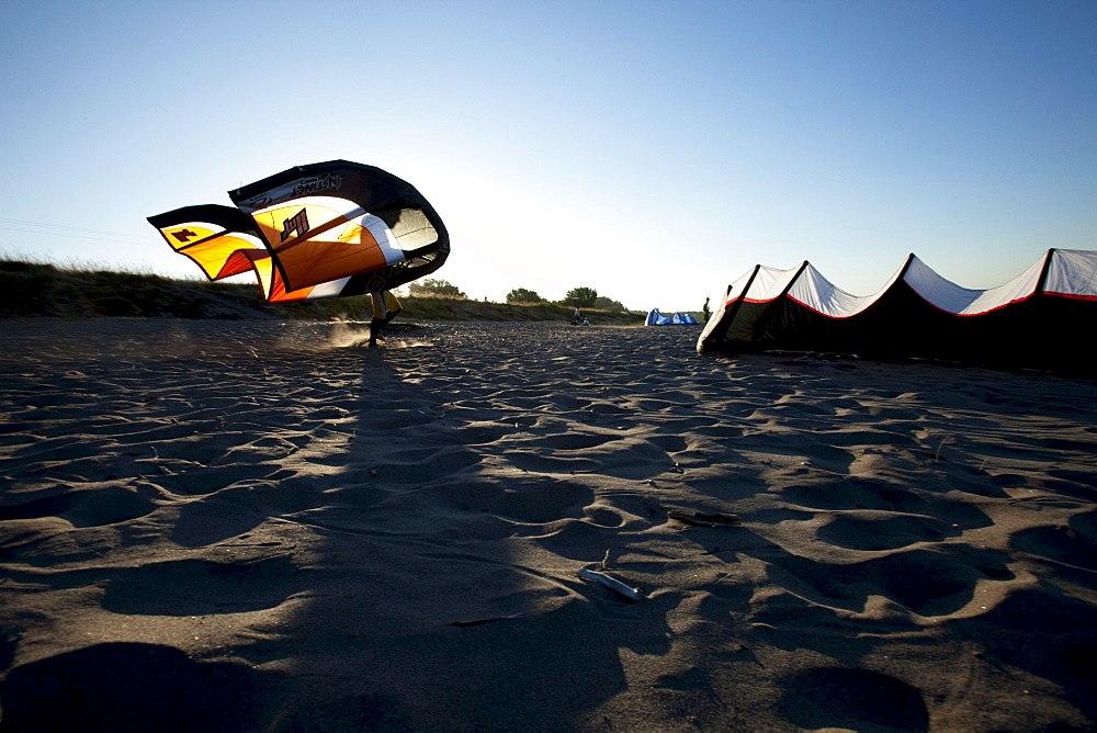 Silhouette of a man walking with a kiteboarding kite on the beach at sunset.