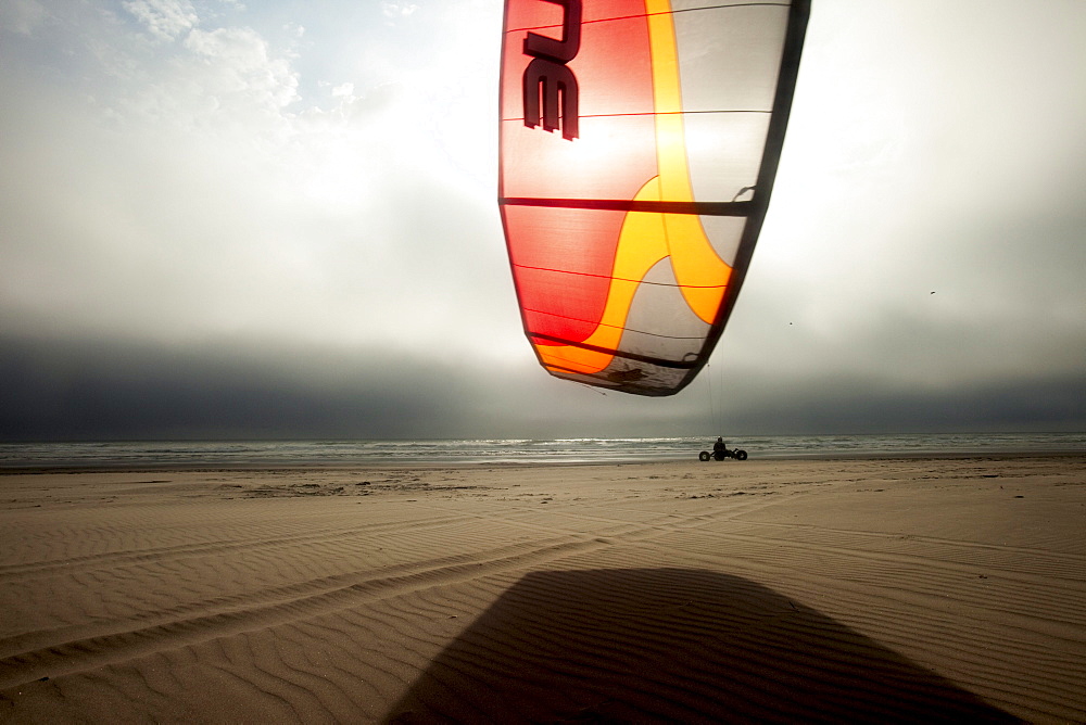 Silhouette of one male kite buggier (kite buggy) rolling down the beach in ominous clouds and unusual light.