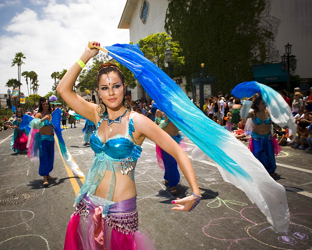 A harem dances up the street at a parade in Santa Barbara. The parade features extravagant floats and costumes.