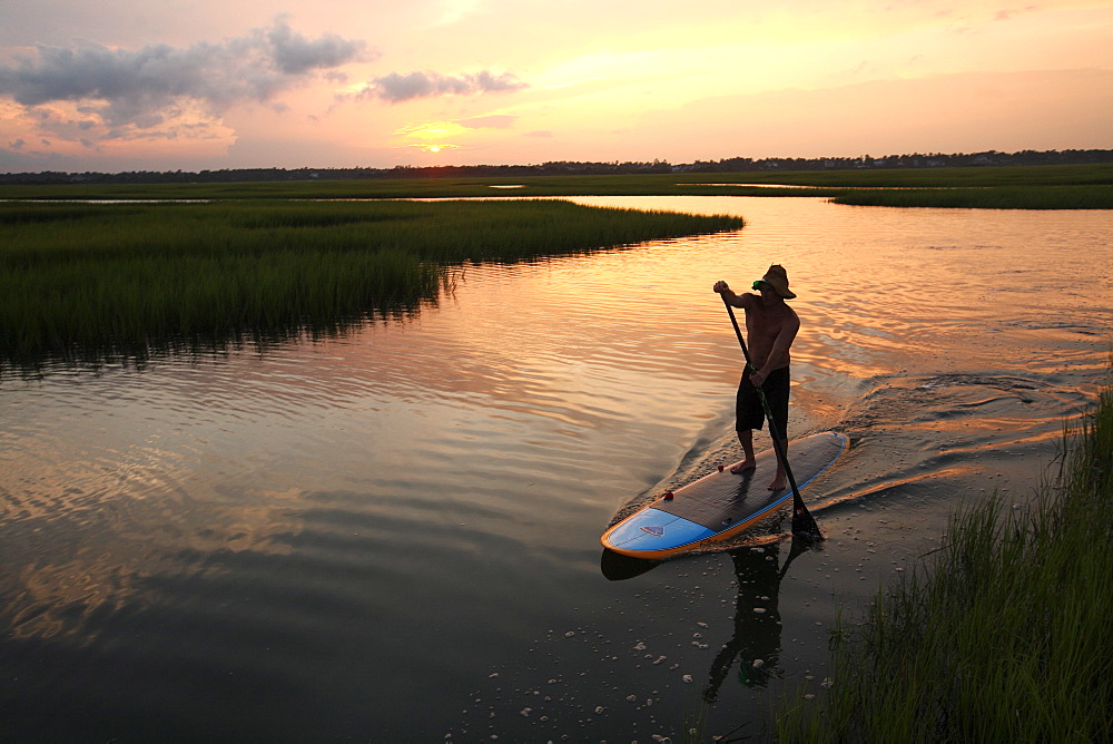 A man stand up paddle boarding in the Marsh