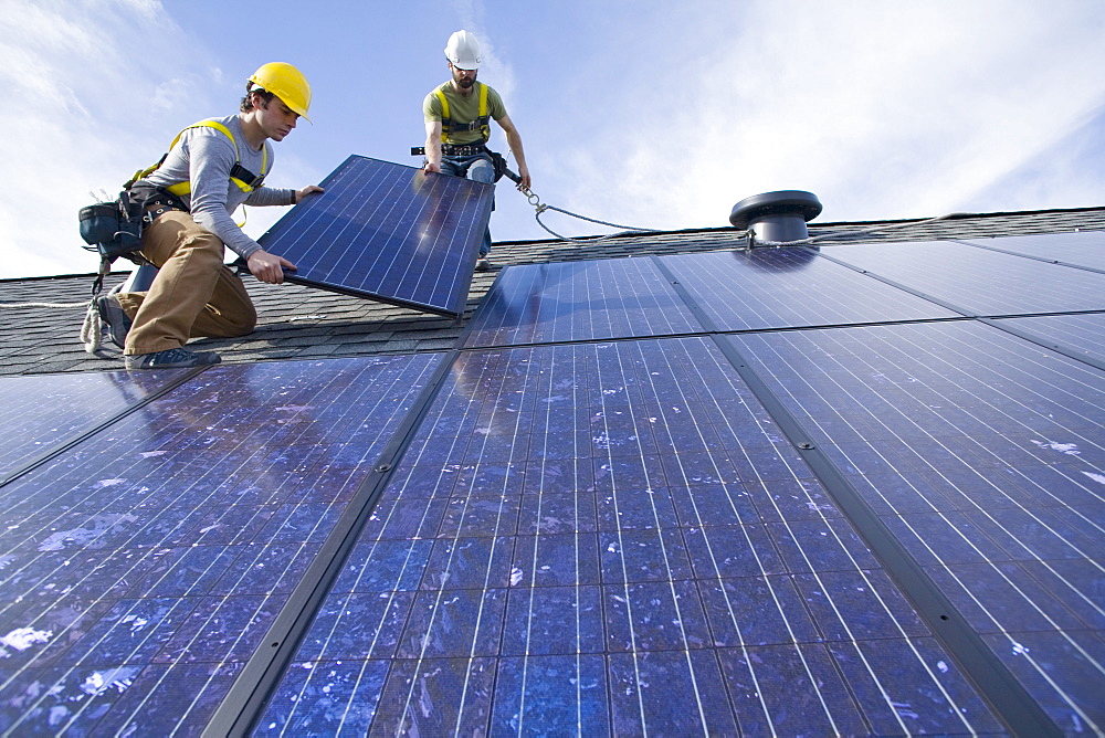 Two workers install solar panels on a rooftop in Redmond, WA.